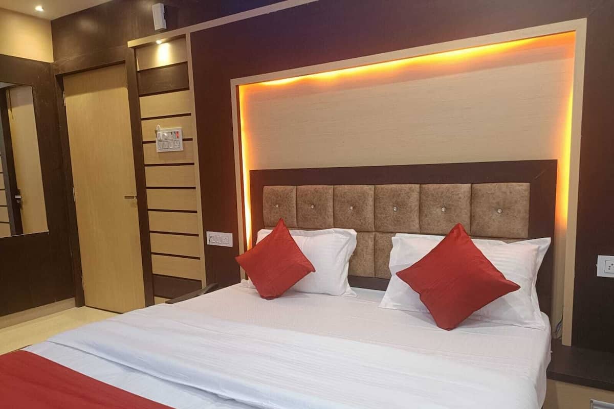 Quarto de hotel com uma cama grande, duas almofadas vermelhas, cabeceira com iluminação embutida e parede revestida de madeira.