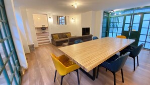 Ein modernes Wohnzimmer mit einem Holzesstisch, gelben und blauen Stühlen, einem Sofa und einer Treppe, die in ein Obergeschoss führt.