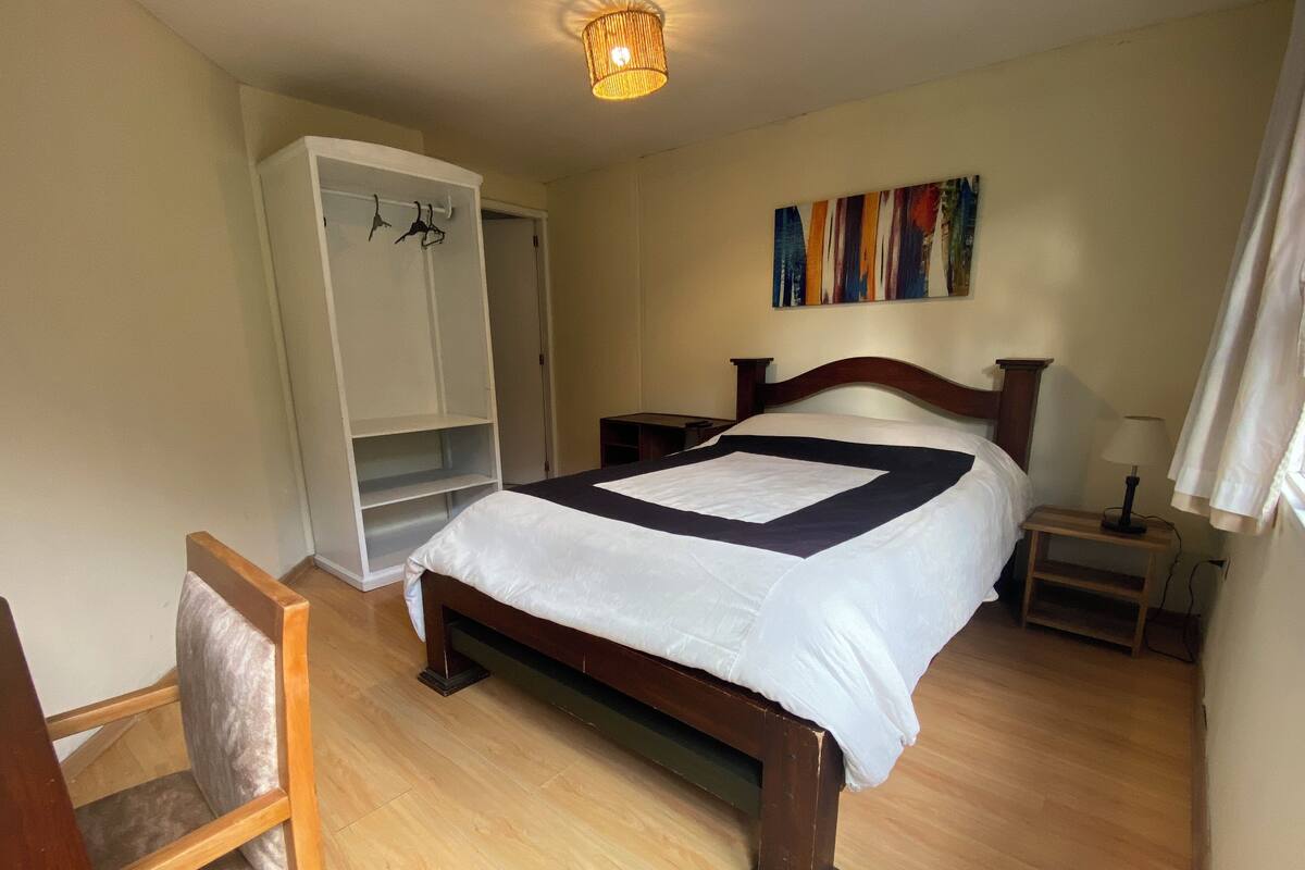 A bedroom with a wooden bed, a wardrobe, a chair, and a bedside table.