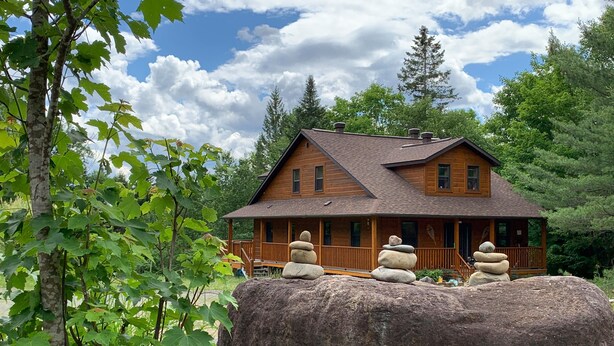 A wooden cabin with a porch and stone stacks. - DOMAINE BONHEURA; A HAVEN OF PEACE SURROUNDED BY NATURE IN ABUNDANCE! (Val-David)