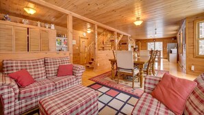 A cozy cabin interior with a plaid sofa set, wooden walls, and a dining area with a table and chairs. - DOMAINE BONHEURA; A HAVEN OF PEACE SURROUNDED BY NATURE IN ABUNDANCE! (Val-David)