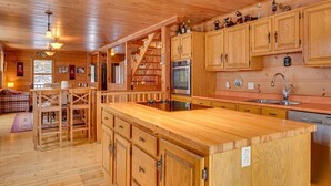 A wooden cabin interior with a kitchen, dining area, and staircase. - DOMAINE BONHEURA; A HAVEN OF PEACE SURROUNDED BY NATURE IN ABUNDANCE! (Val-David)