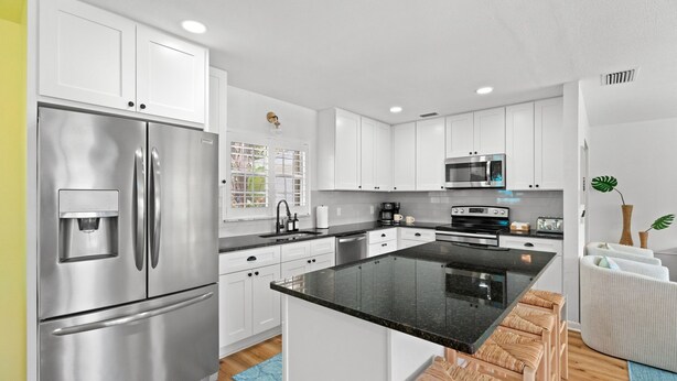 A modern kitchen with white cabinets, stainless steel appliances, a central island with bar stools, and a view of the outdoors through a window. - 5BR~Huge Backyard~Minigolf~Heated Pool~Outdoor Projector~Gameroom~FIOS WiFi (Brandon)