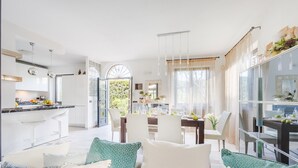 A modern kitchen with white cabinets, a marble countertop, and a dining area with a glass table and chairs.