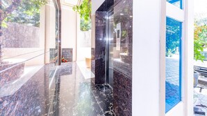 A modern lobby with marble flooring, a glass elevator, and a view of the outdoors. - Magnolia Hotel Cam Ranh (Bac Cam Ranh)