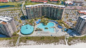 A large hotel with multiple floors, a central swimming pool, and a landscaped area with palm trees.