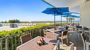 A terrace with outdoor seating, a view of the beach, and a clear sky.