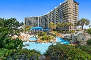 A hotel with a large pool surrounded by rocks and greenery, a covered seating area, and a modern building with multiple balconies. - Edgewater Beach Resort Beachfront Sleeps 8 Golf (Panama City Beach)