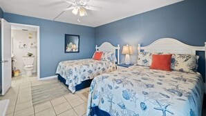 A bedroom with two beds, a ceiling fan, and a bathroom visible in the background.
