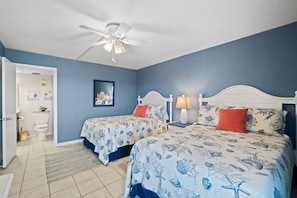 A bedroom with two beds, a ceiling fan, and a bathroom visible in the background.