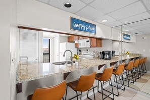 A kitchen with a long counter, bar stools, a microwave, and a coffee maker.