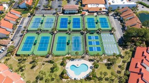 An aerial view of a property with multiple tennis courts, a swimming pool, and surrounding greenery.