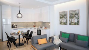 A modern kitchen with white cabinets, a dining area with a round table and chairs, and a grey sofa with green cushions.
