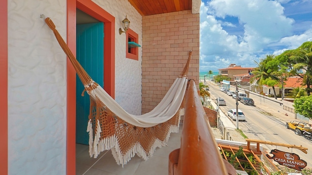 A hammock on a balcony with a view of a street and buildings. - CASA MANOA POUSADA (Maragogi)
