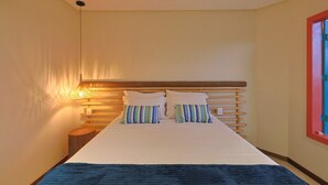 A bedroom with a bed, bedside lamp, and a window with a red frame. - CASA MANOA POUSADA (Maragogi)