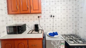 A compact kitchen with wooden cabinets, a microwave, a gas stove, and patterned tiles. - Lux Suites Cabre Apartments (Nakuru)