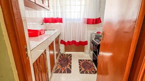 A narrow hallway leading to a bathroom with a sink, mirror, and red and white curtains. - Lux Suites Cabre Apartments (Nakuru)