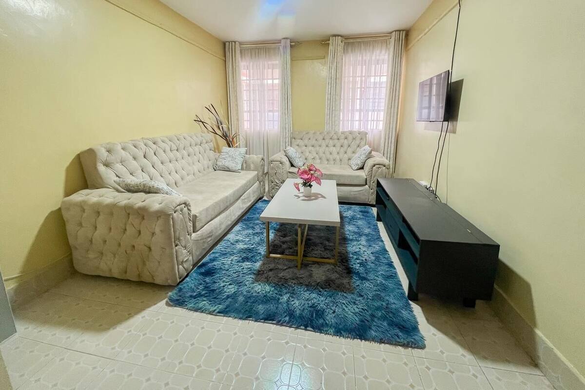 A living room with two beige sofas, a small white table with a vase, a blue rug, and a black cabinet.