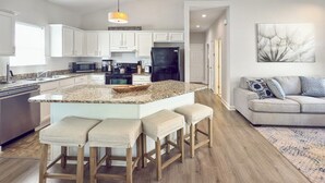 A modern kitchen with white cabinets, a granite countertop, and a black refrigerator. There are three wooden stools at the island.