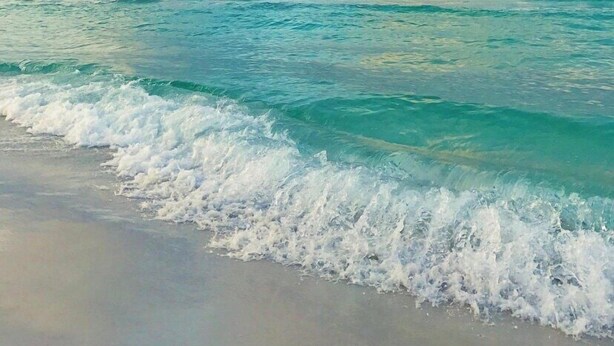 A beach with turquoise water and white waves.