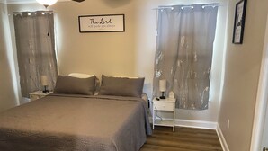 A bedroom with a large bed, two bedside tables with lamps, a ceiling fan, and a wall with a framed inspirational quote.
