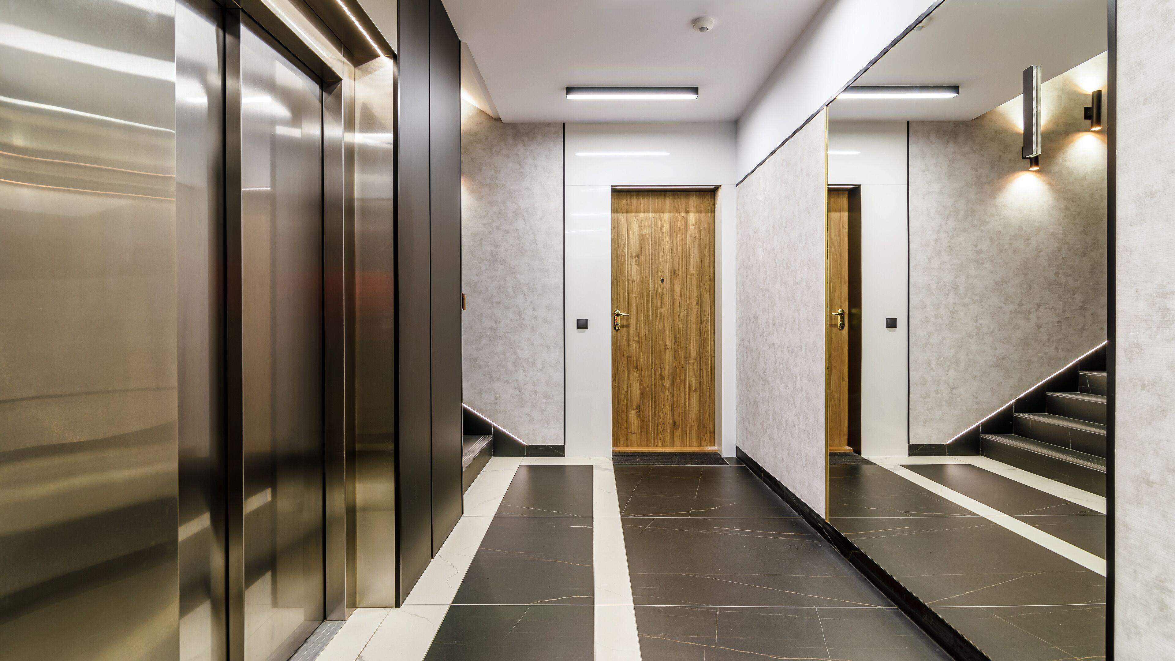 A modern hallway with a marble floor, a wooden door, and a staircase with black steps.