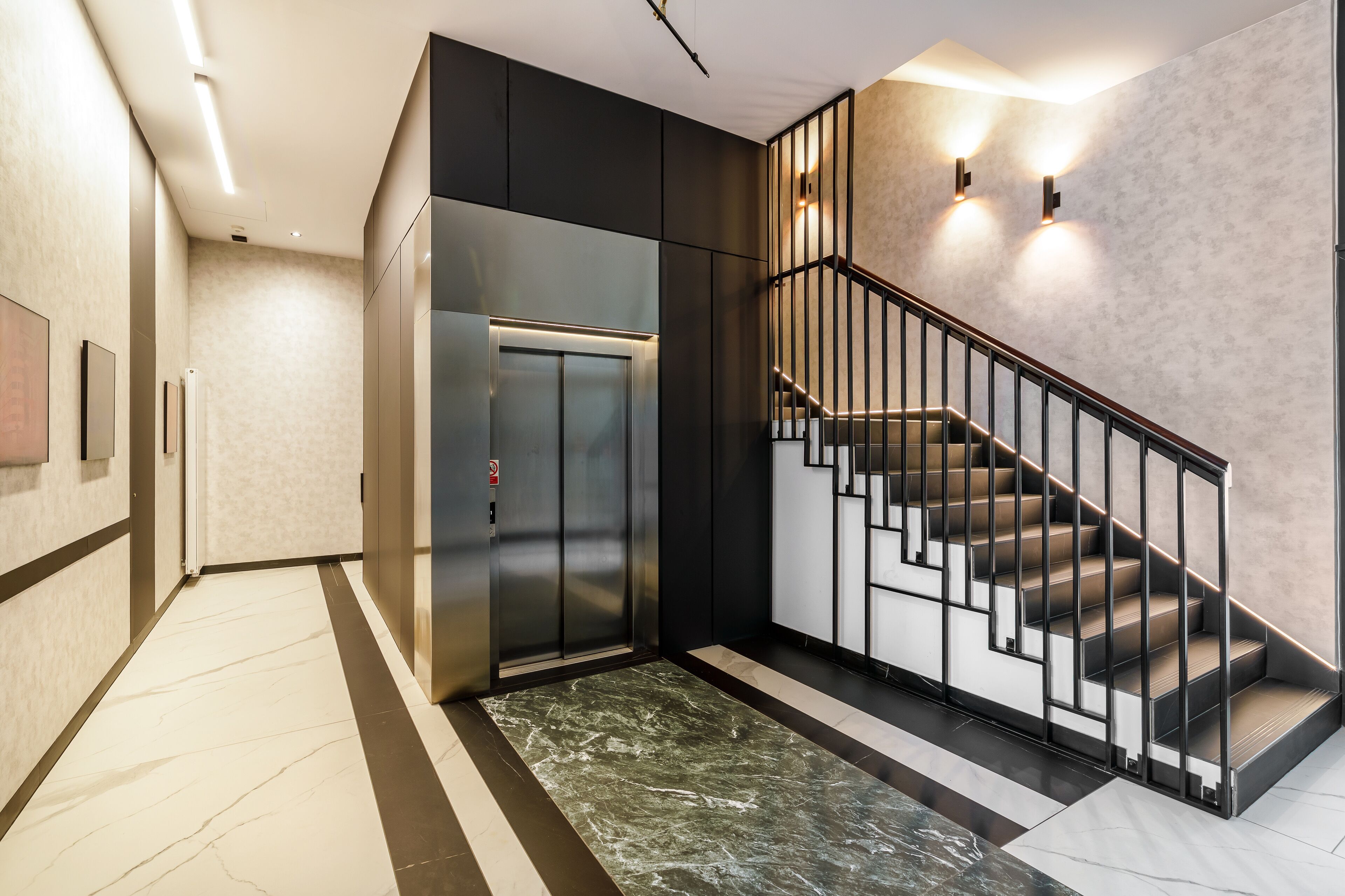 A modern elevator, a staircase with a metal railing, and a patterned carpet.
