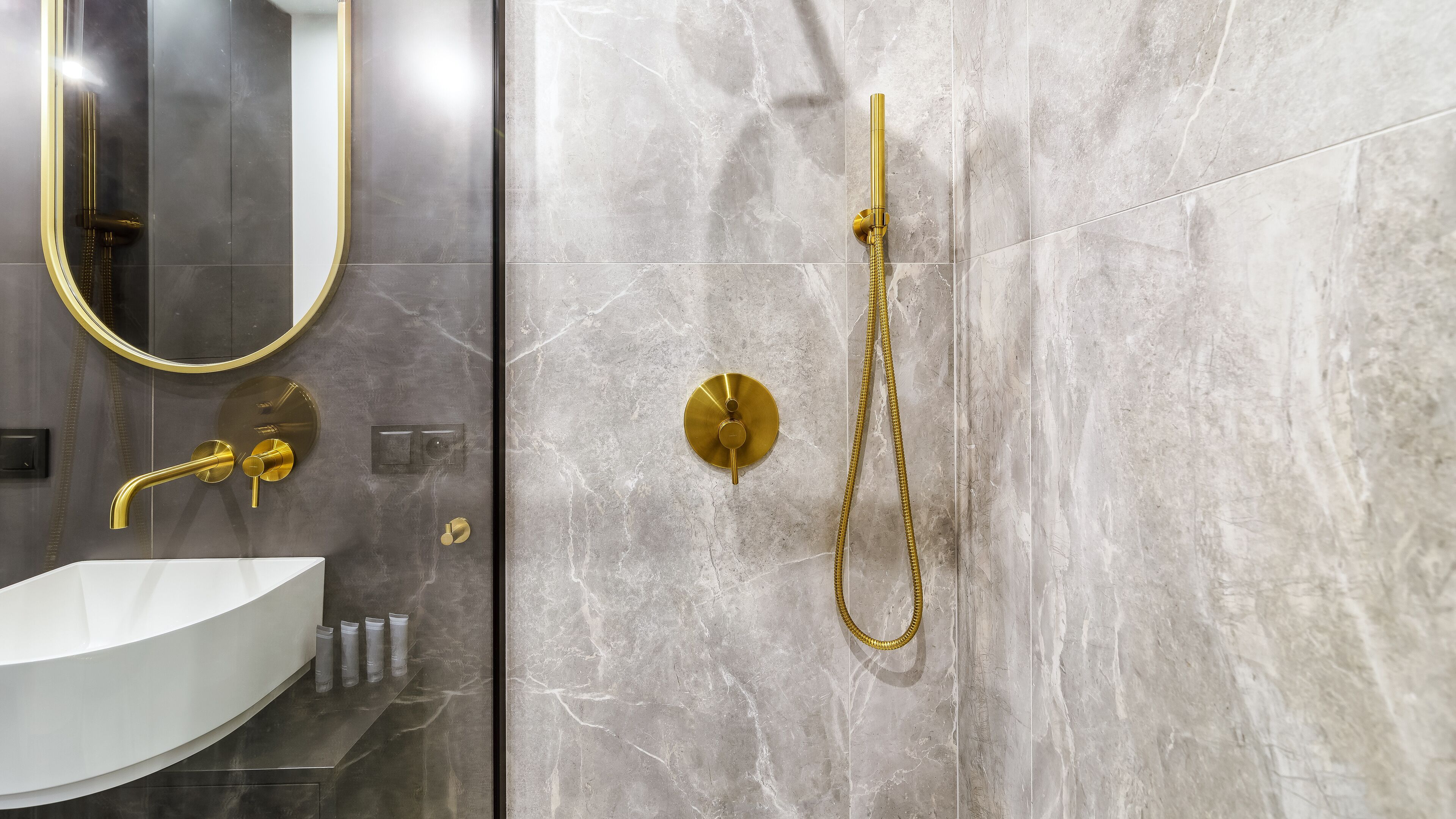 Une salle de bain moderne avec un lavabo blanc, des robinetteries dorées et des murs en marbre.