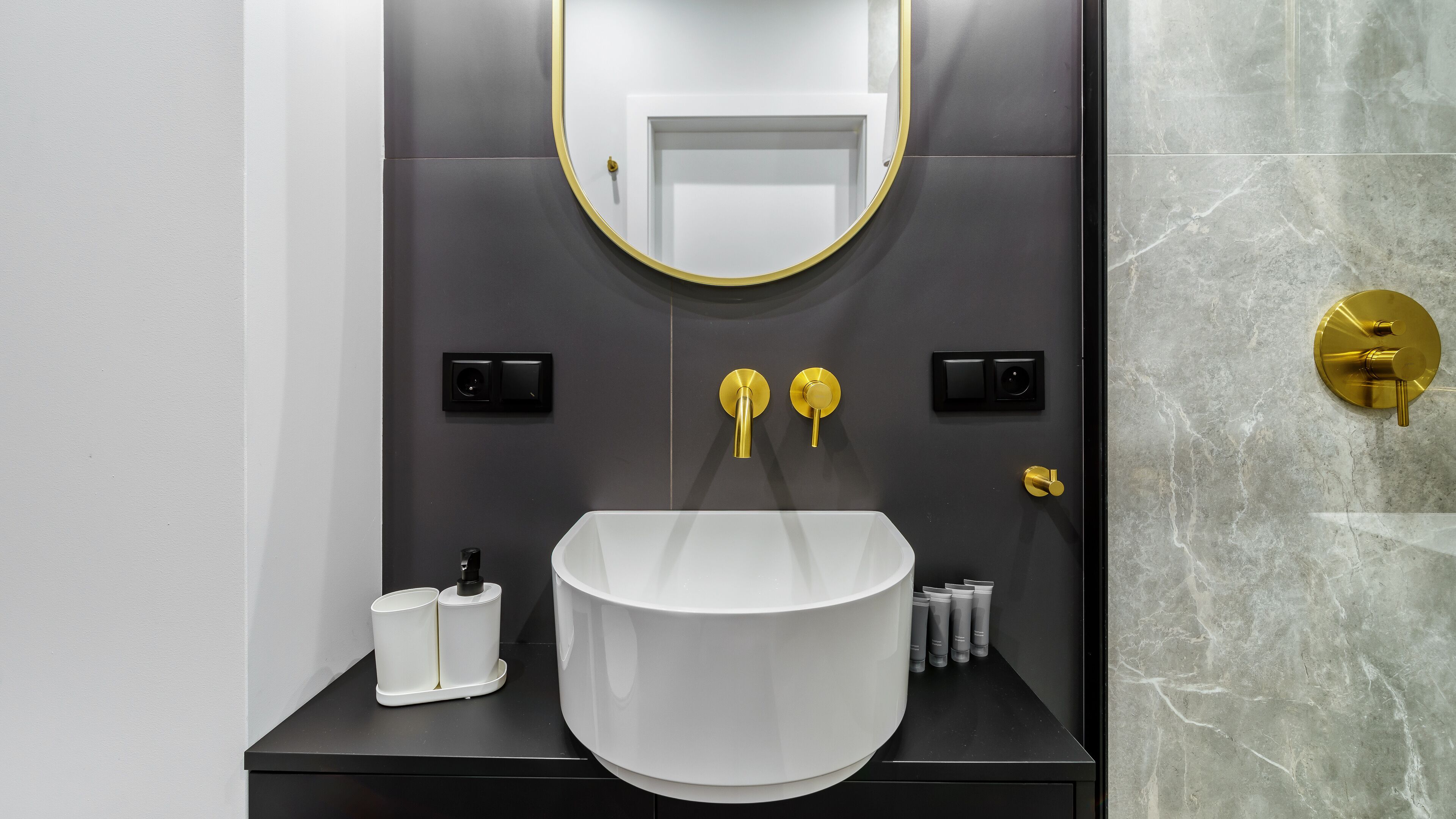 Ein modernes Badezimmer mit einem weißen Waschbecken, goldenen Armaturen und einer Marmorwand.