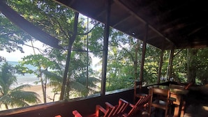 A beachside seating area with a view of the ocean and palm trees. -  Pirate Drake Beach Hostel (Drake Bay)