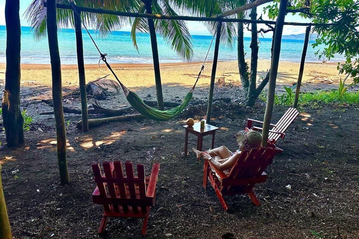 Eine Strandansicht mit einer Hängematte, zwei roten Stühlen und einem kleinen Tisch.