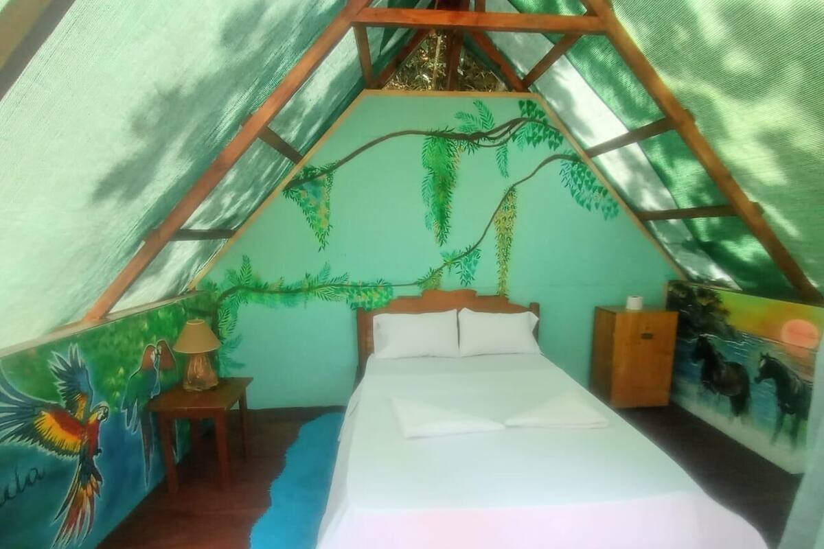 Ein Zelttraum mit Bett, Lampe und einem Wandbild von Papageien.