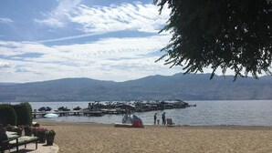 Een strand met een tent, ligbedden en een steiger met boten.