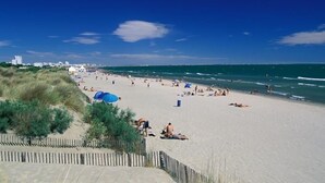 Una playa con gente tomando el sol y nadando, una orilla arenosa y un cielo azul despejado.