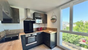 Una cocina moderna con armarios oscuros, un microondas, una cafetera roja y un ventanal con vistas a zonas verdes y edificios.