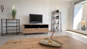 Una sala de estar con una mesa de centro de madera, un televisor sobre un mueble de madera, una planta y una estantería.