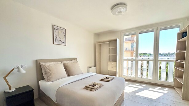 Un dormitorio con cama, lámpara de noche y vistas al exterior.