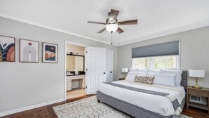 Ein Schlafzimmer mit einem Bett, einem Deckenventilator, einem Fenster und einer Tür zu einem Badezimmer.