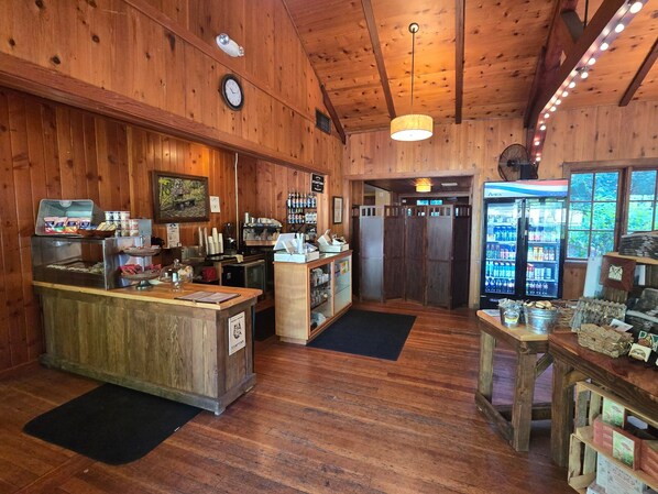 A rustic wooden interior with a coffee station, a refrigerator stocked with beverages, and a wooden counter with various items. - Smith Creek Village (Sublimity)