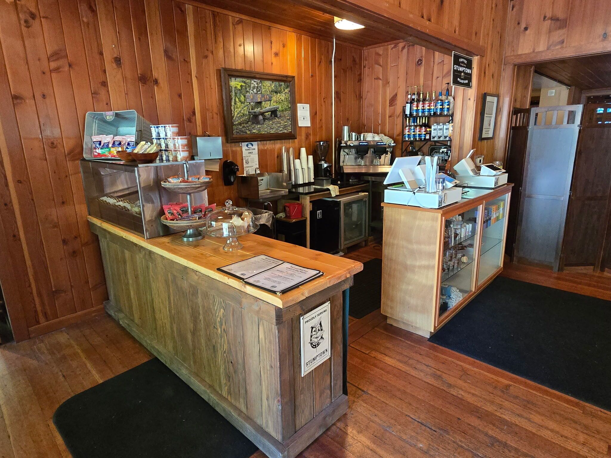 A wooden interior with a reception desk, a coffee station, and a display of snacks.