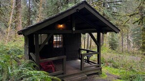 A rustic cabin with a porch, a small table, and a single window. - Smith Creek Village  (Sublimity)