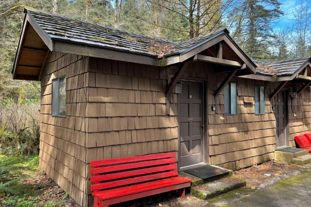 A wooden cabin with a front door, a bench, and a small porch area.