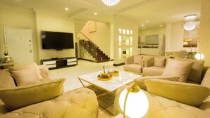 A spacious living room with a large flat-screen TV, a staircase, and a dining area with a chandelier.