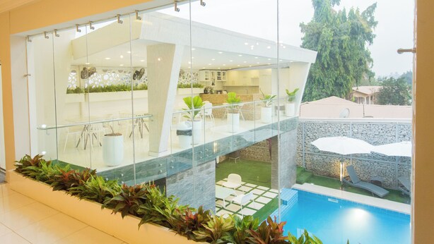 A modern house with a glass-enclosed balcony overlooking a swimming pool and garden.