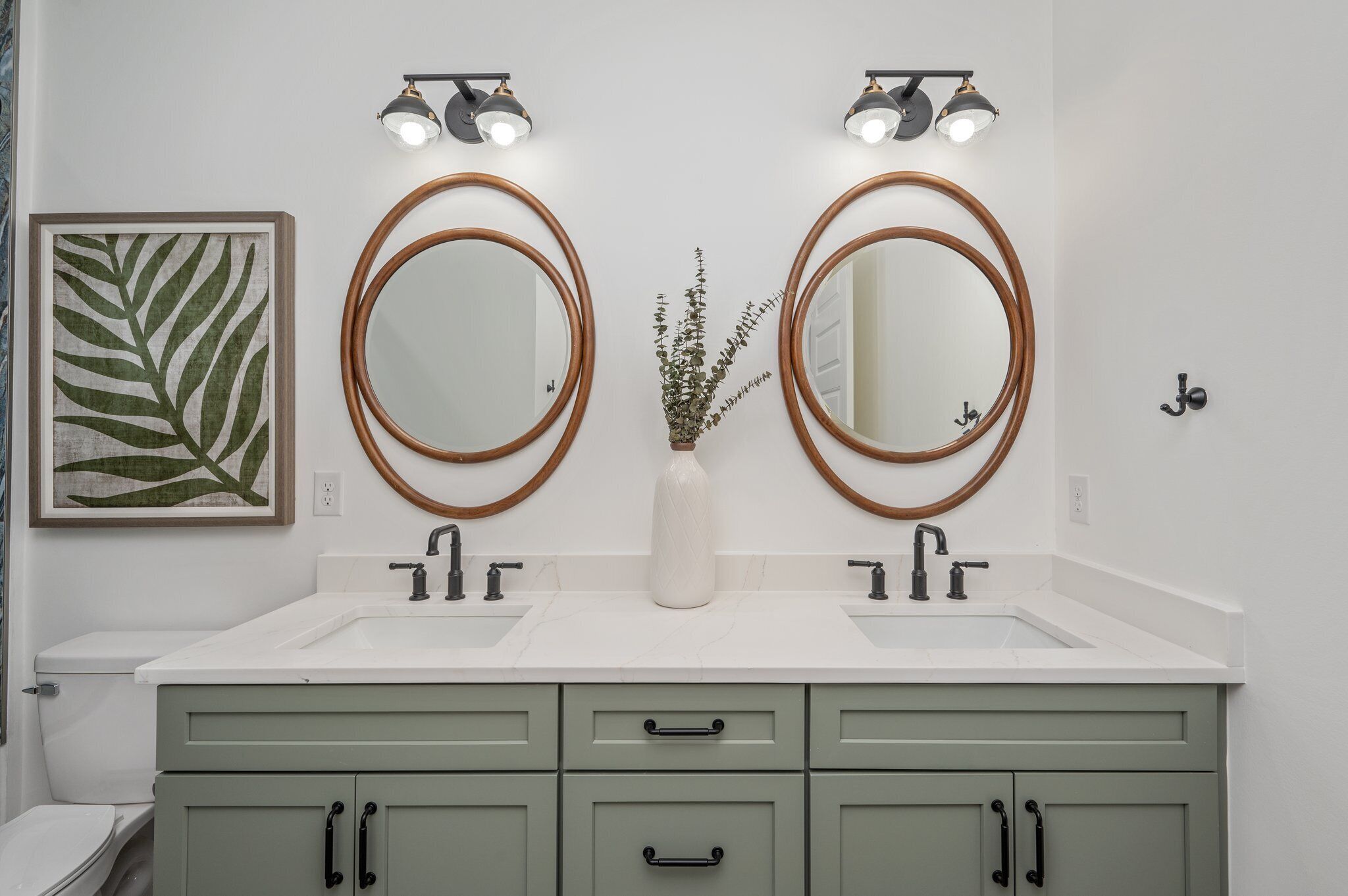 A bathroom with two round mirrors, a white sink, and a green vanity.
