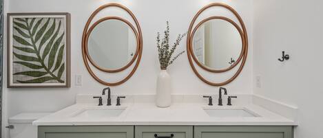 A bathroom with two round mirrors, a white sink, and a green vanity.