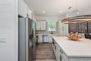 A modern kitchen with white cabinetry, a stainless steel refrigerator, a dishwasher, and a large island with a bowl. - Reefwood - Sleeps 21 - 2 Blocks to the Beach! (Destin)