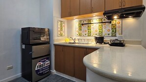 A compact kitchen with wooden cabinets, a built-in oven, and a countertop with a sink and stove. - Cozy 1-bedroom condo with AC and WiFi in central Davao City (Davao City)