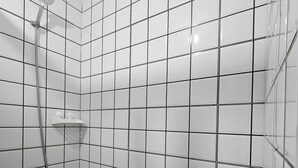 A bathroom with white tiled walls, a shower with a handheld showerhead, a blue bucket, and a small shelf. - Cozy 1-bedroom condo with AC and WiFi in central Davao City (Davao City)