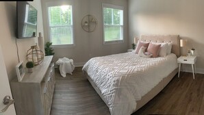 A bedroom with a large bed, a nightstand, a lamp, a TV, and a window with blinds. - 3-bedroom bungalow in charming Easley with AC, WiFi (Easley)